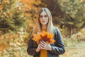 schattig smiley vrouw Holding herfst bladeren in vallen park. seizoensgebonden, levensstijl en vrije tijd concept. foto