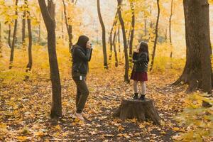 moeder nemen afbeelding haar charismatisch dochter Aan retro camera in herfst park. hobby's en vrije tijd concept. foto