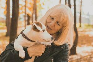 portret senior glimlachen vrouw knuffelen haar hond in herfst park. actief veroudering en huisdier concept. foto