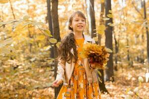 weinig kind meisje met herfst oranje bladeren in een park. levensstijl, vallen seizoen en kinderen concept. foto