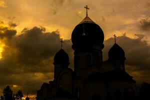 de silhouet van de koepels van een orthodox christen kerk in Roemenië tegen de achtergrond van de rood lucht. geloof of religie concept foto