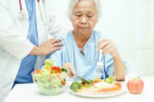 Aziatisch ouderen vrouw geduldig aan het eten Zalm inzet en groente salade voor gezond voedsel in ziekenhuis. foto
