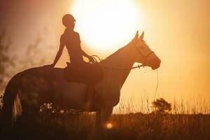 de silhouet van een paard rijder en haar paard tegen de achtergrond van zonsondergang. foto