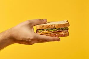 hand- Holding smakelijk belegd broodje Aan een geel achtergrond. ai gegenereerd foto