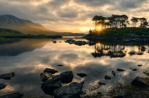 dramatisch bewolkt oever van het meer landschap zonsopkomst landschap van twaalf dennen eiland weerspiegeld in water omringd door bergen Bij derryclare, Connemara nationaal park in provincie Galway, Ierland foto