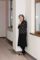 oud vrouw van 80 jaren oud blijft dichtbij naar de venster foto