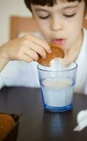 jongen van zes jaren is nemen een glas van warm melk met haver koekjes. foto