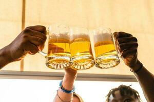 klein groep van jong volwassen multi-etnisch vrienden roosteren met drie mokken van bier foto