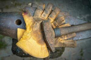 detailopname van vuil handschoenen en hamer over- een aambeeld van smid foto