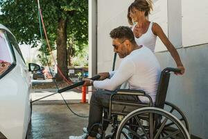 gelukkig midden- oud paar met Mens zittend Aan rolstoel het wassen auto Bij openbaar auto wassen foto