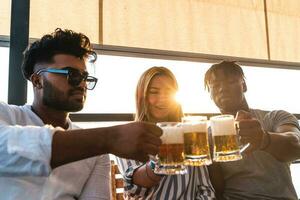 klein groep van jong volwassen multi-etnisch vrienden roosteren met drie mokken van bier foto