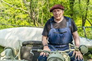 portret van volwassen smid. arbeider ontspannende Aan zijn oud motorfiets in de platteland foto