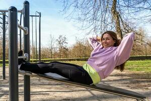 portret van jong vrouw aan het doen buik spieren training Aan een bank buitenshuis foto