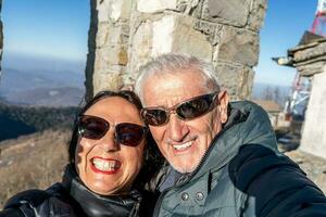 midden- oud paar vervelend winter kleren nemen een selfie over- een berg foto