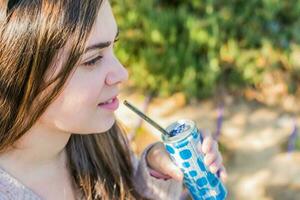 jong vrouw drinken een Frisdrank, buitenshuis, zonnig dag. foto