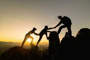 silhouet van wandelaars beklimming omhoog berg klif. beklimming groep helpen elk andere terwijl beklimming omhoog in zonsondergang. concept van helpen en teamwerk. foto