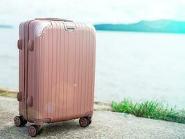 een pastel roze koffer gelegd uit in de achtergrond is een wazig visie van de zee Aan een zonnig dag. geschikt voor gaan Aan vakantie foto