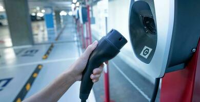 hand- Holding elektrisch oplader Bij een elektrisch voertuig opladen station. reclame ev auto opladen punt voor in rekening brengen ev accu. elektrisch voertuig opladen station Bij kelder auto parkeren veel van de winkelcentrum foto