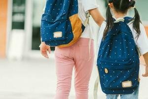 terug visie van twee schoolmeisjes Holding rugzakken terwijl wandelen in gang foto