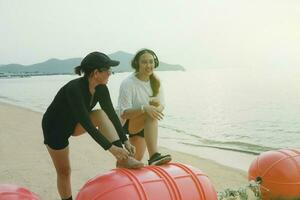 twee Aziatisch vrouw uitrekken voordat oefening Aan zee strand foto