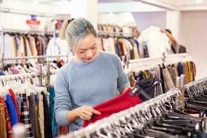 elegant Aziatisch vrouw is kiezen de tweede hand- trui van de kleding winkel voor winter seizoen mode naar houden warm Bij de nieuw jaar en Kerstmis vakantie foto