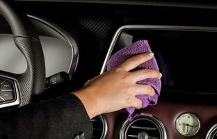 een jong vrouw hand- met een Purper microfiber kleding schoonmaak de scherm binnen een luxueus auto foto