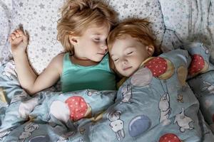 twee kleine zusjes en zusjes die in een omhelzing in bed slapen onder één deken foto