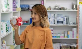 vrouw staand in een apotheek op te slaan en Holding een geneeskunde doos lezing etiket instructies Aan de pakket, klant buying kiezen pillen, gezondheidszorg concepten. foto