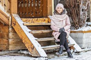 warm geklede jonge vrouw die zich voordeed op de veranda van een houten huis in het dorp. wintervakanties op het platteland foto