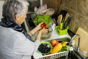 senior vrouw Bij huis het wassen en desinfecteren fruit en groenten. foto