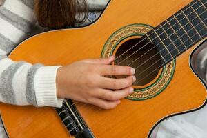 hand- van een weinig meisje aan het leren naar Speel de gitaar Bij haar huis foto