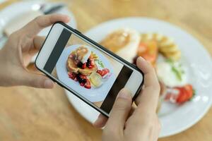 restaurant eigenaar duurt een afbeelding van de voedsel Aan de tafel met een smartphone naar post Aan een website. online voedsel levering, bestellen onderhoud, beïnvloeder, opnieuw bekijken, sociaal media, deel, marketing, interesse. foto