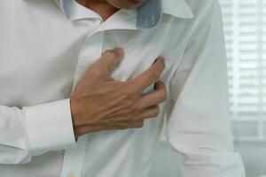 hand- houden borst met hart aanval symptomen, Aziatisch Mens hebben borst pijn veroorzaakt door hart ziekte, lek, dilatatie, vergroot coronaire hart, druk op Aan de borst met een pijnlijk uitdrukking foto
