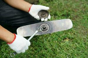 dichtbij omhoog foto van handen slijtage handschoenen van een monteur zijn repareren en vastdraaien de blad van gras maaien machine. concept , onderhoud agrarisch machine.