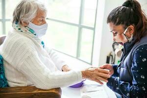 senior vrouw krijgen een manicure Bij huis gedurende covid 19 pandemisch vervelend gezicht masker foto