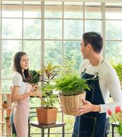 tuinman jong Aziatisch Mens vrouw twee persoon familie staan glimlachen kijk en helpen organiseren klein boom. binnen kamer boom blad groen in kalmte werk winkel huis fabriek . hobby baan gelukkig en zorg concept foto