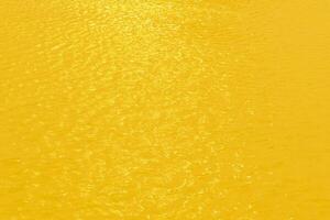 geel water met rimpelingen Aan de oppervlak. onscherp wazig transparant goud gekleurde Doorzichtig kalmte water oppervlakte structuur met spatten en bubbels. water golven met schijnend patroon structuur achtergrond. foto
