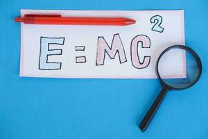 papier kaart van formule emc2 Aan kleurrijk boeken met pennen en vergroten glas. concept, Einstein formule. massa energie gelijkwaardigheid. opleiding, fysica onderwerp. foto