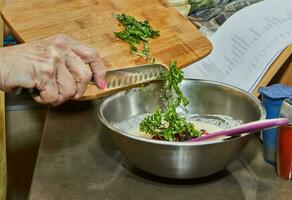 chef gooit basilicum bladeren Aan houten snijdend bord met mes in schotel foto