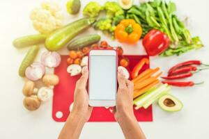 kijken voor een recept Aan de internet met mobiel telefoon gebaseerd Aan groente ingrediënten foto
