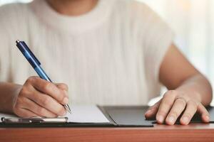 Aziatisch vrouw hand- Holding een pen en schrijven iets Aan de notitieboekje foto