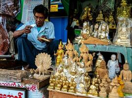 Yangon, Myanmar - jan 5, 2020 een beeldhouwer zit verkoop houten producten gesneden in de het formulier van Boeddha en mooi Birmees goden. foto