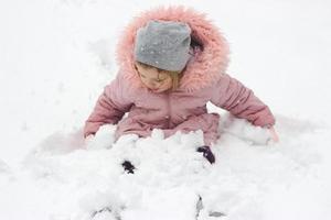klein meisje zit in de sneeuw en speelt met verse sneeuw die 's nachts is gevallen
