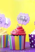 smakelijke aardbei cupcakes in kleurrijke papieren bakbekers, met gelukkige verjaardag wenskaart, op gele achtergrond. feest achtergrond foto