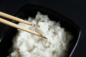 kom met gekookte rijst op zwarte achtergrond. Aziatisch eten en bamboe eetstokjes.