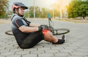 fietser met knie pijn buitenshuis. mannetje fietser zittend Aan de bestrating met knie pijn. concept van een fietser met knie letsel buitenshuis foto