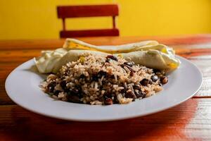 gallo pinto met quesillo geserveerd Aan houten tafel. Nicaraguaanse galopperen met quesillo Aan de tafel. typisch Nicaraguaanse voedingsmiddelen foto