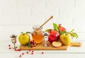 een pot van honing en spil Aan een houten bord met rijp fruit, granaatappels en appels. traditioneel voedsel voor de vakantie van Rosh hasjana. voorkant visie foto