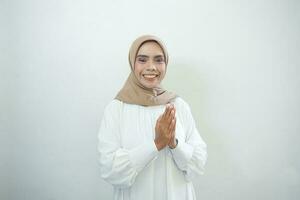jong Aziatisch Islam vrouw vervelend hoofddoek geeft groet handen Bij met een groot glimlach Aan haar gezicht. Indonesisch vrouw Aan grijs achtergrond. eid mubarak, eid fitr, Ramadan foto