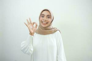 glimlachen jong Aziatisch vrouw in wit gewoontjes tonen Oke gebaar demonstreert symbool van goedkeuring geïsoleerd over- wit achtergrond foto